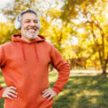 mature man with broad smile in headphones while doing sport in city park