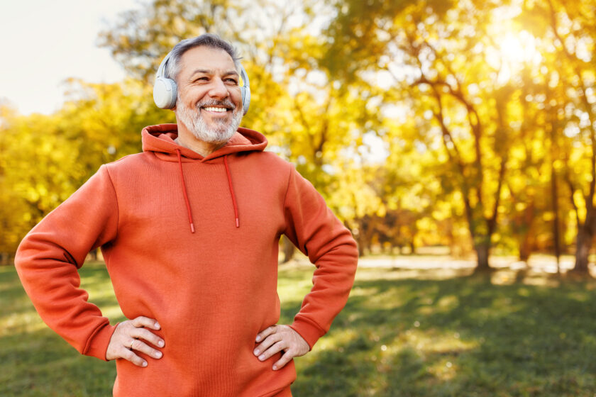 mature man with broad smile in headphones while doing sport in city park