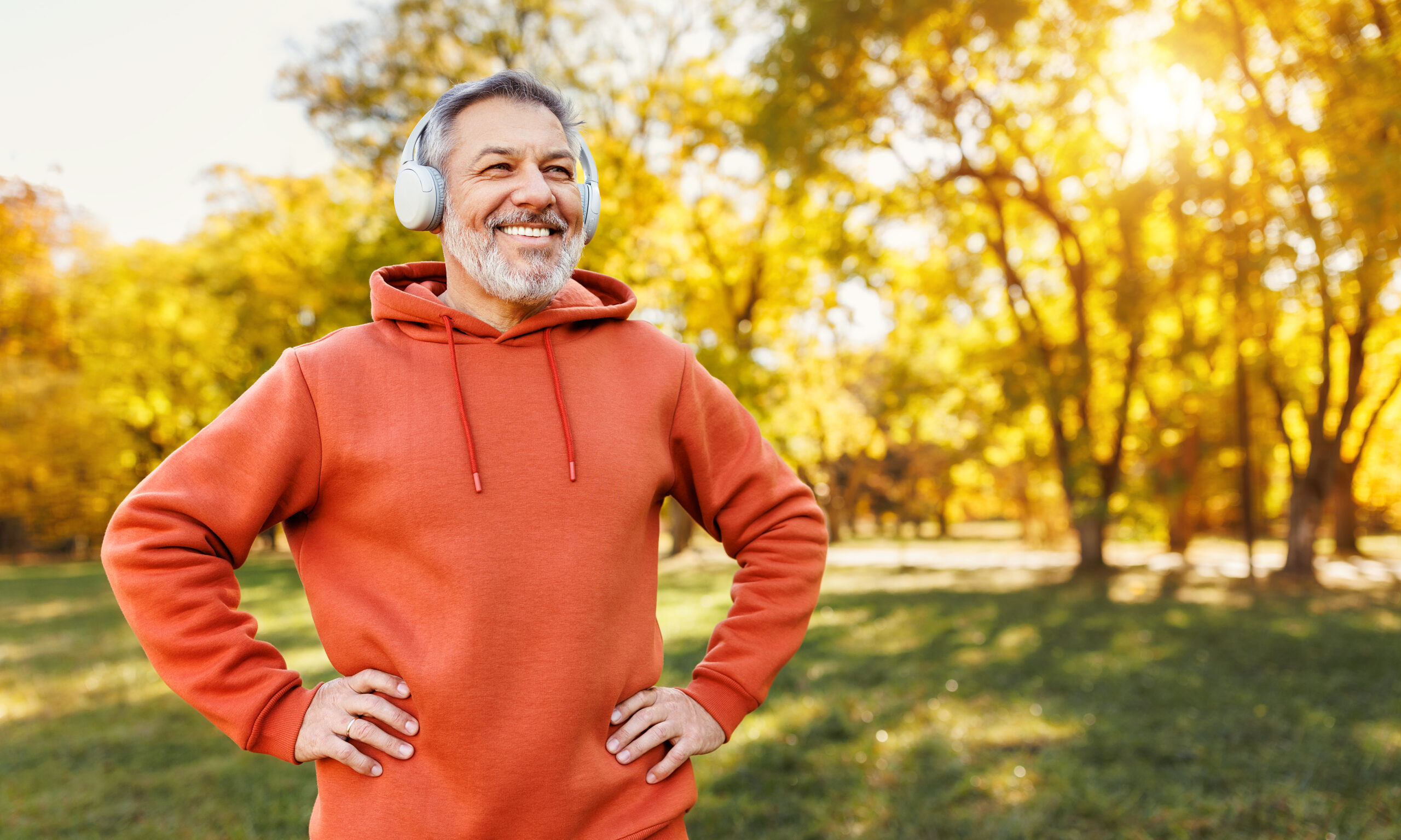 mature man with broad smile in headphones while doing sport in city park