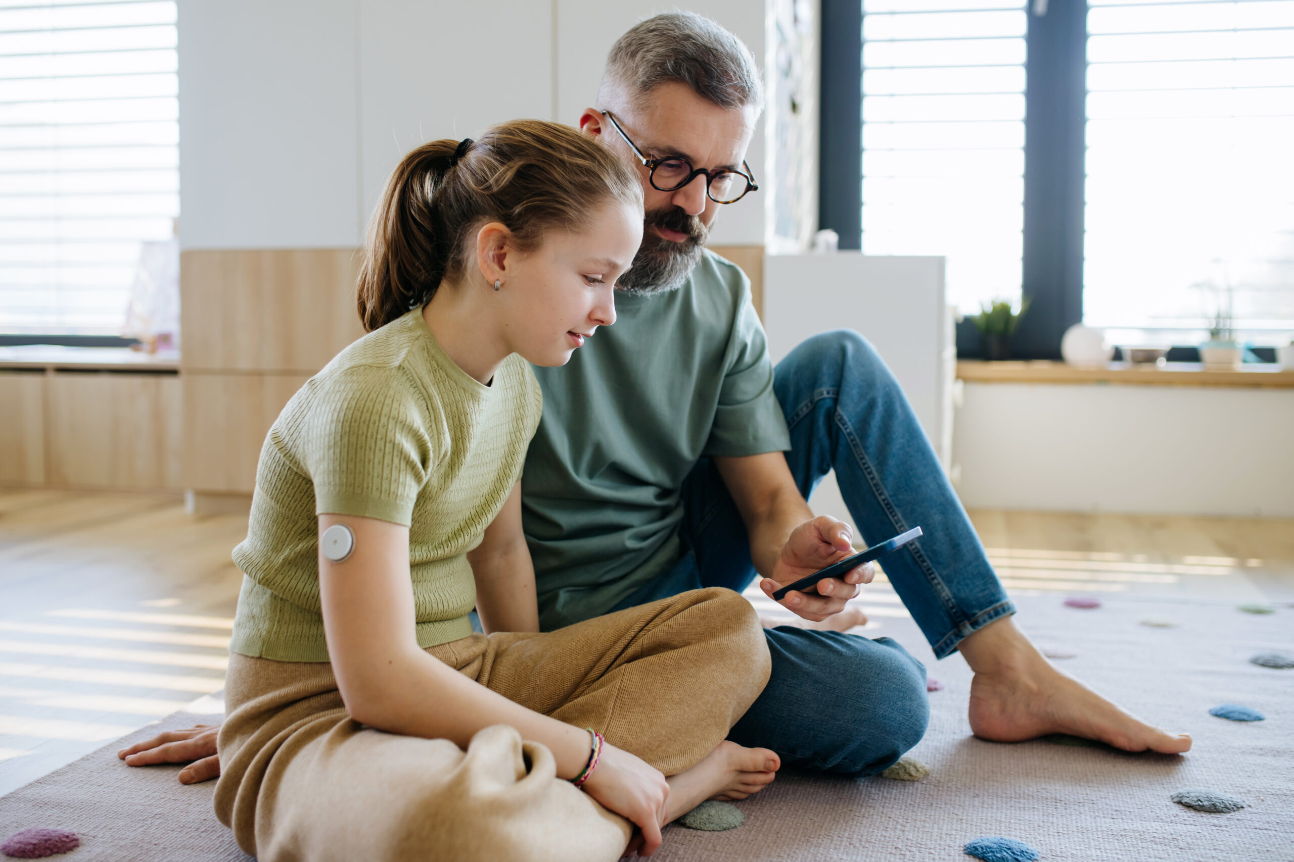 Diabetic girl with a CGM sensor on her arm. Father using an app to monitor blood sugar levels.