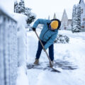 Senior man in warm casual clothes cleaning the empty street from snow with snow shovel