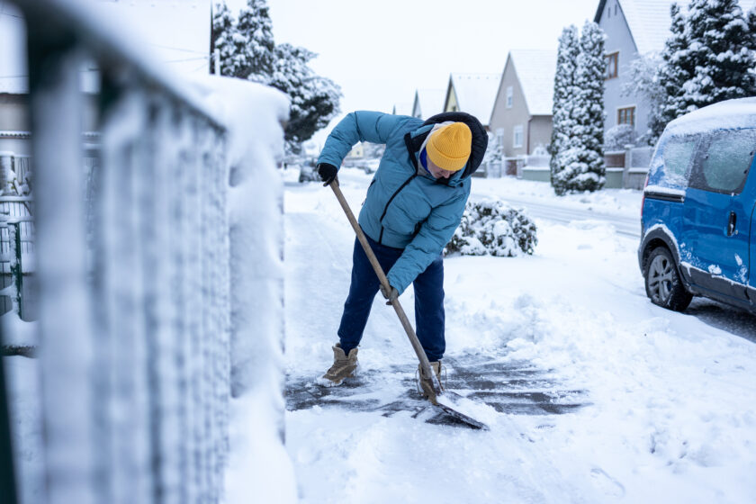 Senior man in warm casual clothes cleaning the empty street from snow with snow shovel
