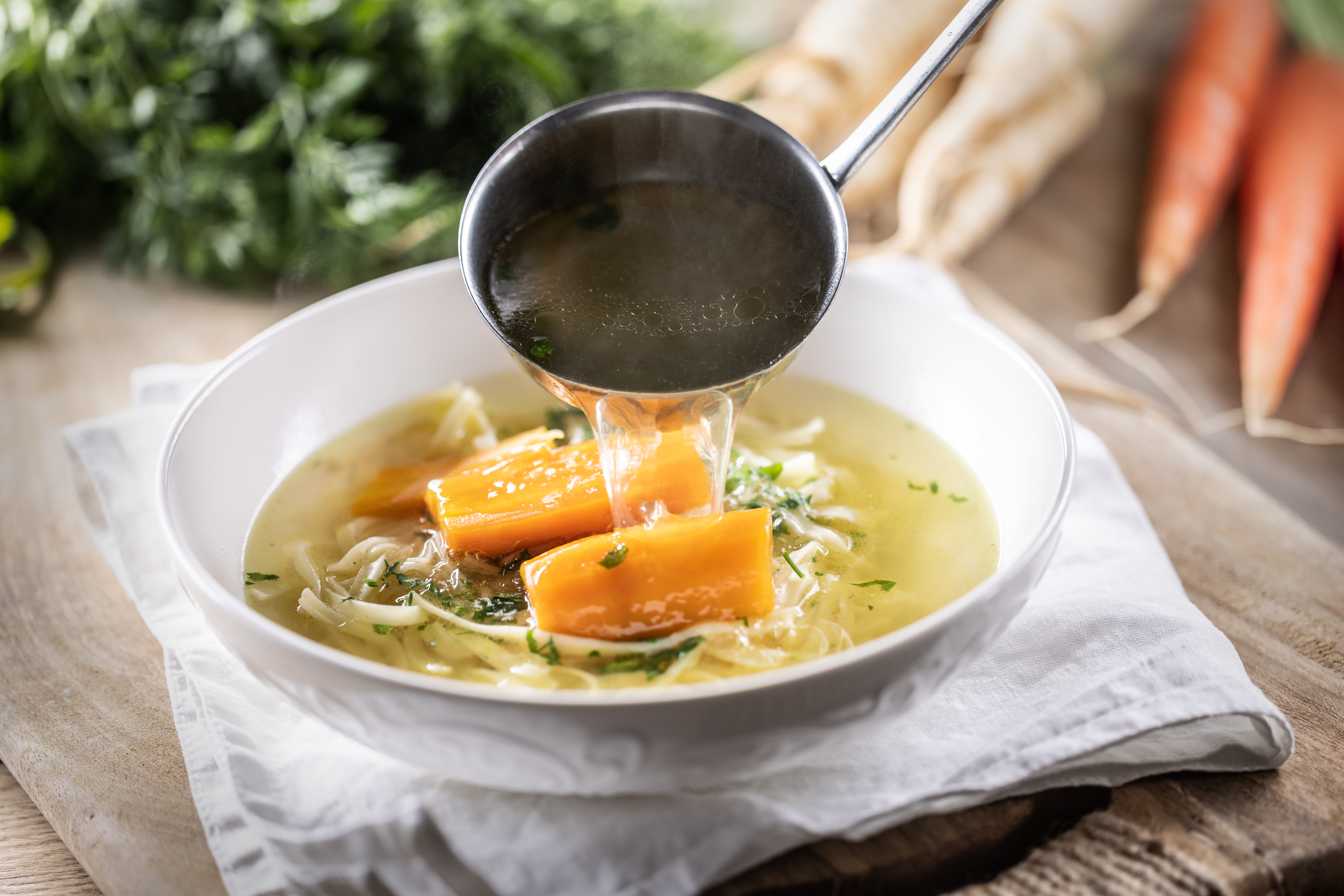 Photo of pouring broth into a bowl of chicken soup.