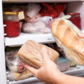 A hand putting two loafs of wheat and brown bread in reserve on a shelf of a home freezer.
