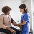 Nurse checking senior woman's blood pressure in exam room