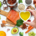 Hand holding heart shaped bowl filled with olive oil on blurred healthy ingredients background