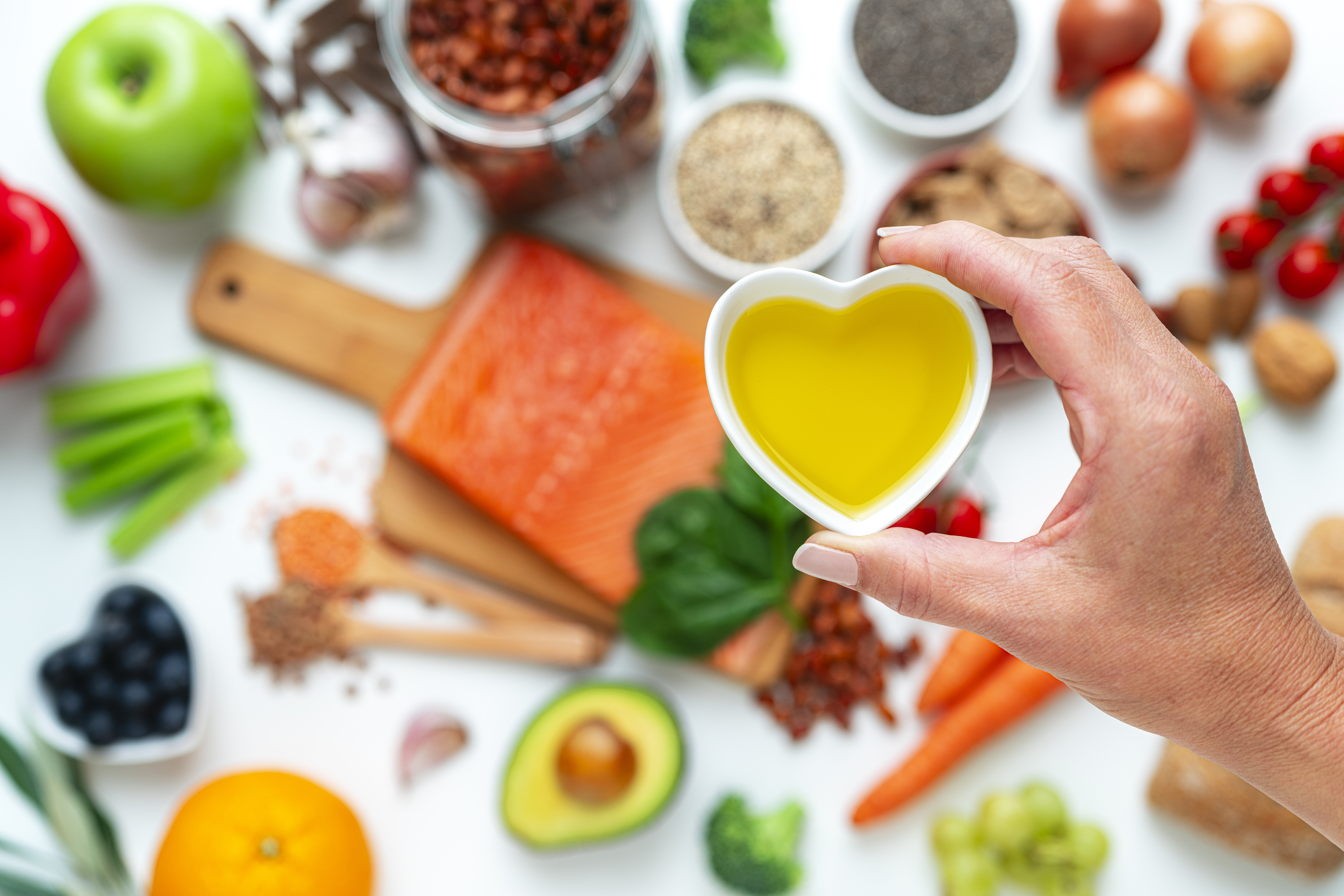 Hand holding heart shaped bowl filled with olive oil on blurred healthy ingredients background