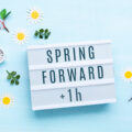 Summer back concept. White Alarm Clock and Spring Daisy Flowers on Blue Background