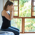 Photoof a woman sitting on the bed suffering from severe headache holding her head at home