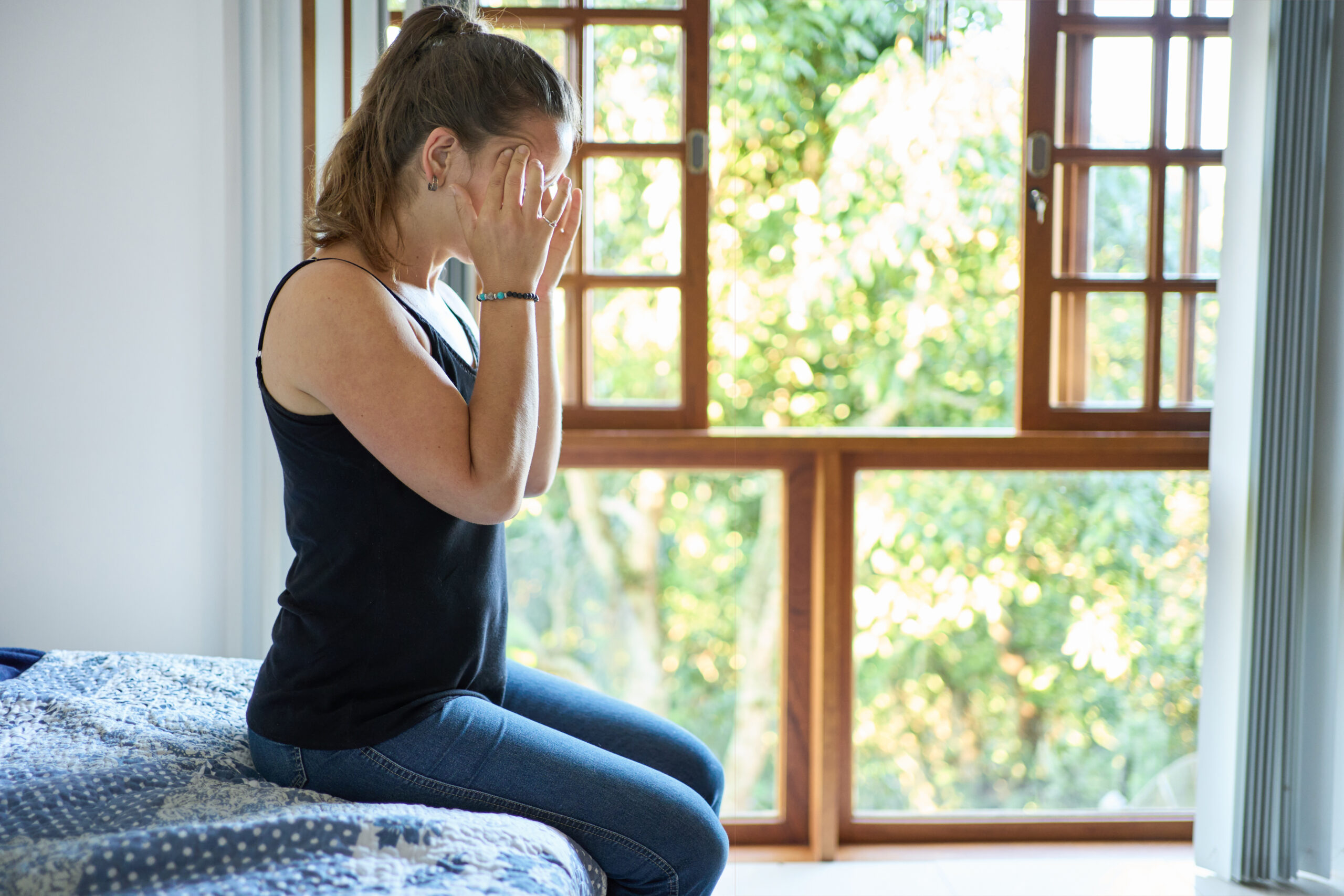 Photoof a woman sitting on the bed suffering from severe headache holding her head at home