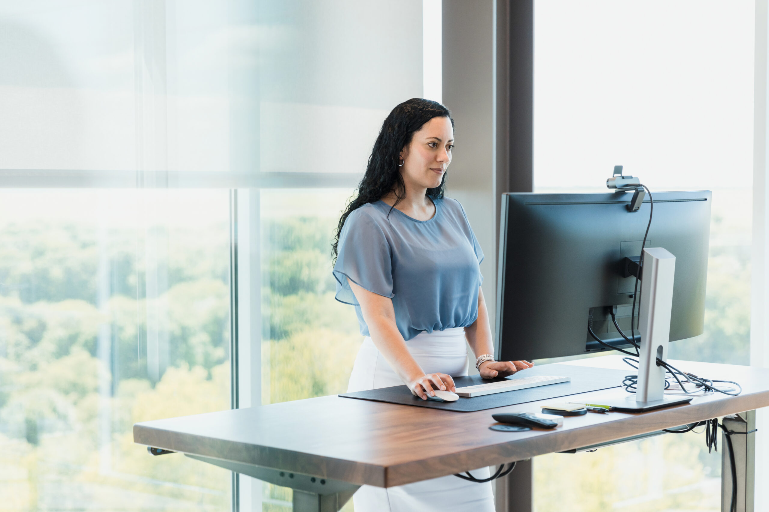 Using a standing desk, the adult female works on her computer in her office.