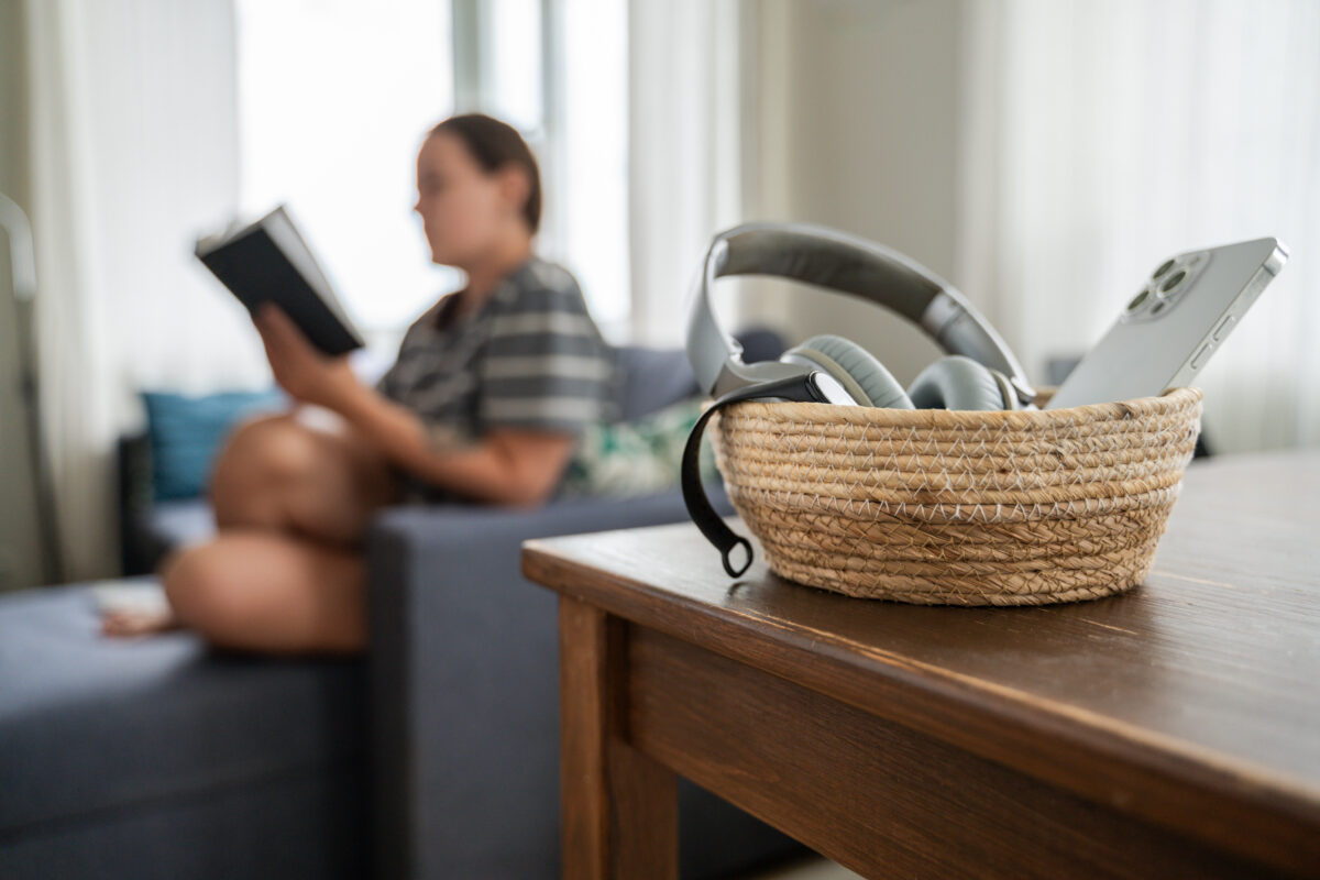 Woman reading book while smartphone is in a basket