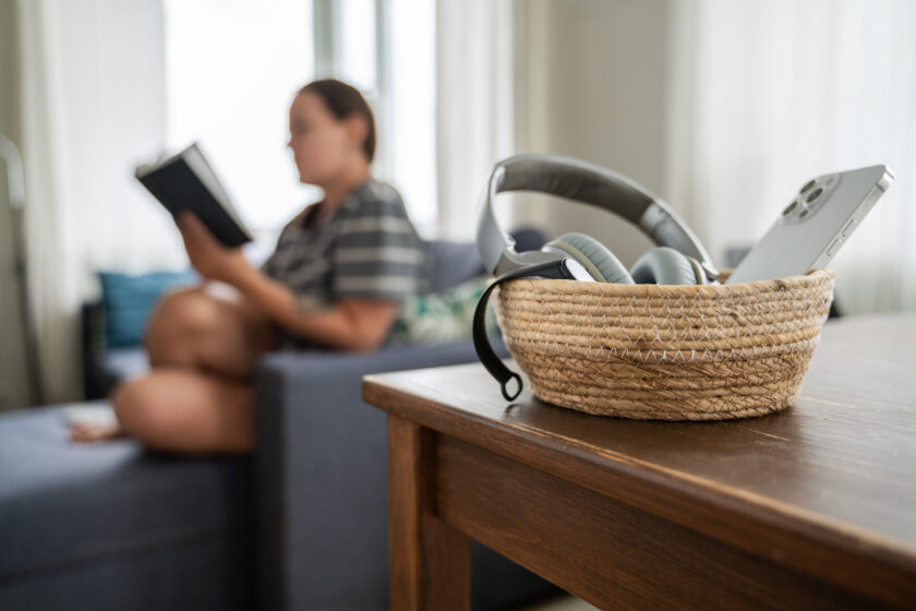 Woman reading book while smartphone is in a basket