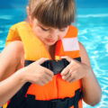 Little girl putting on orange life vest in swimming pool