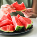 sliced watermelon on a plate with person's hand holding one piece that has a bite taken out of it.