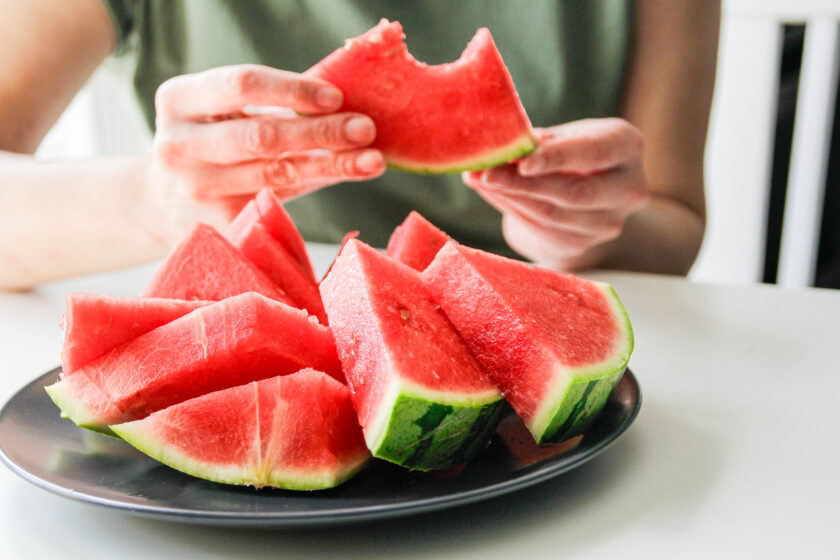 sliced watermelon on a plate with person's hand holding one piece that has a bite taken out of it.