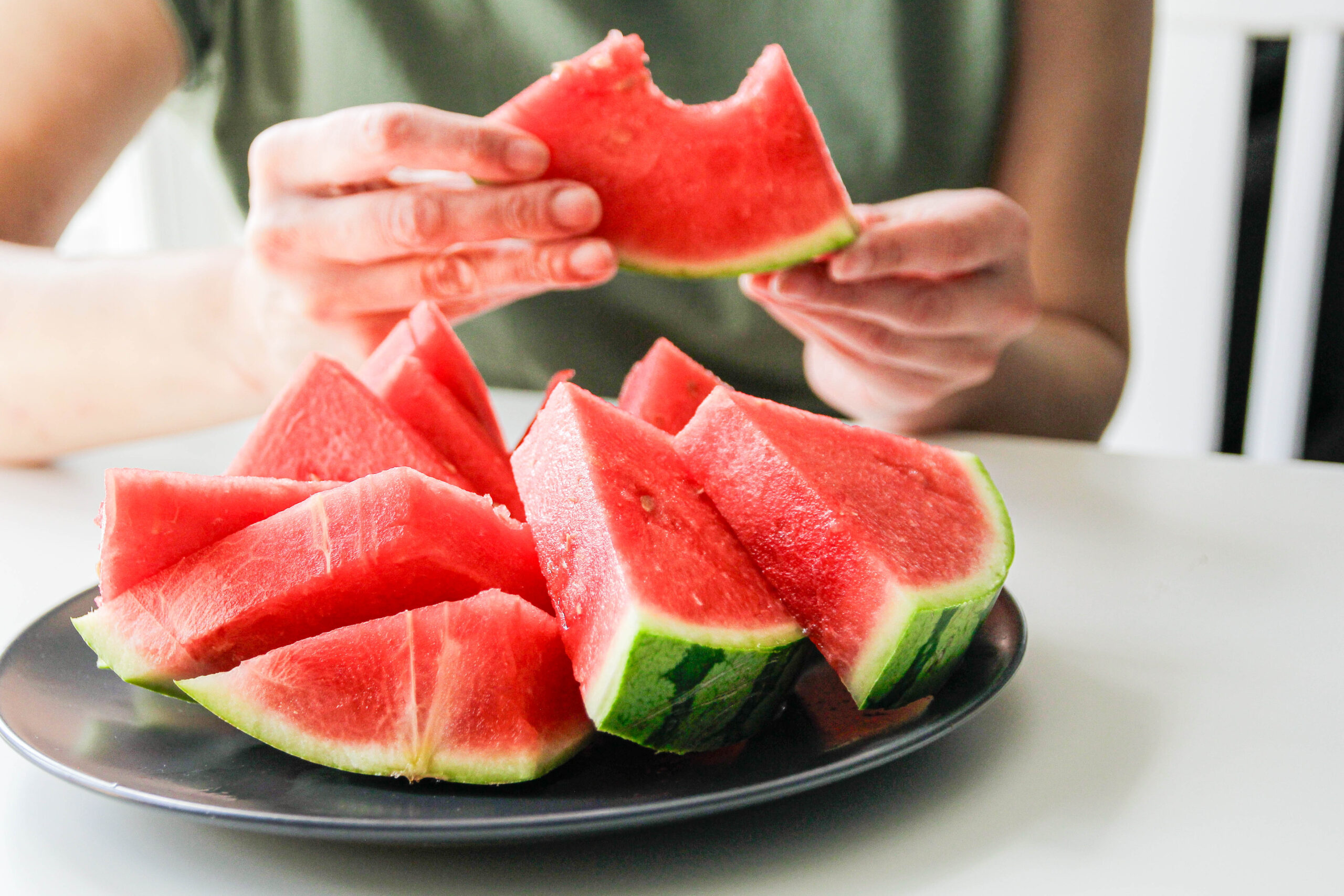 sliced watermelon on a plate with person's hand holding one piece that has a bite taken out of it.