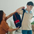 Young mother helps her son prepare his backpack in the living room for school
