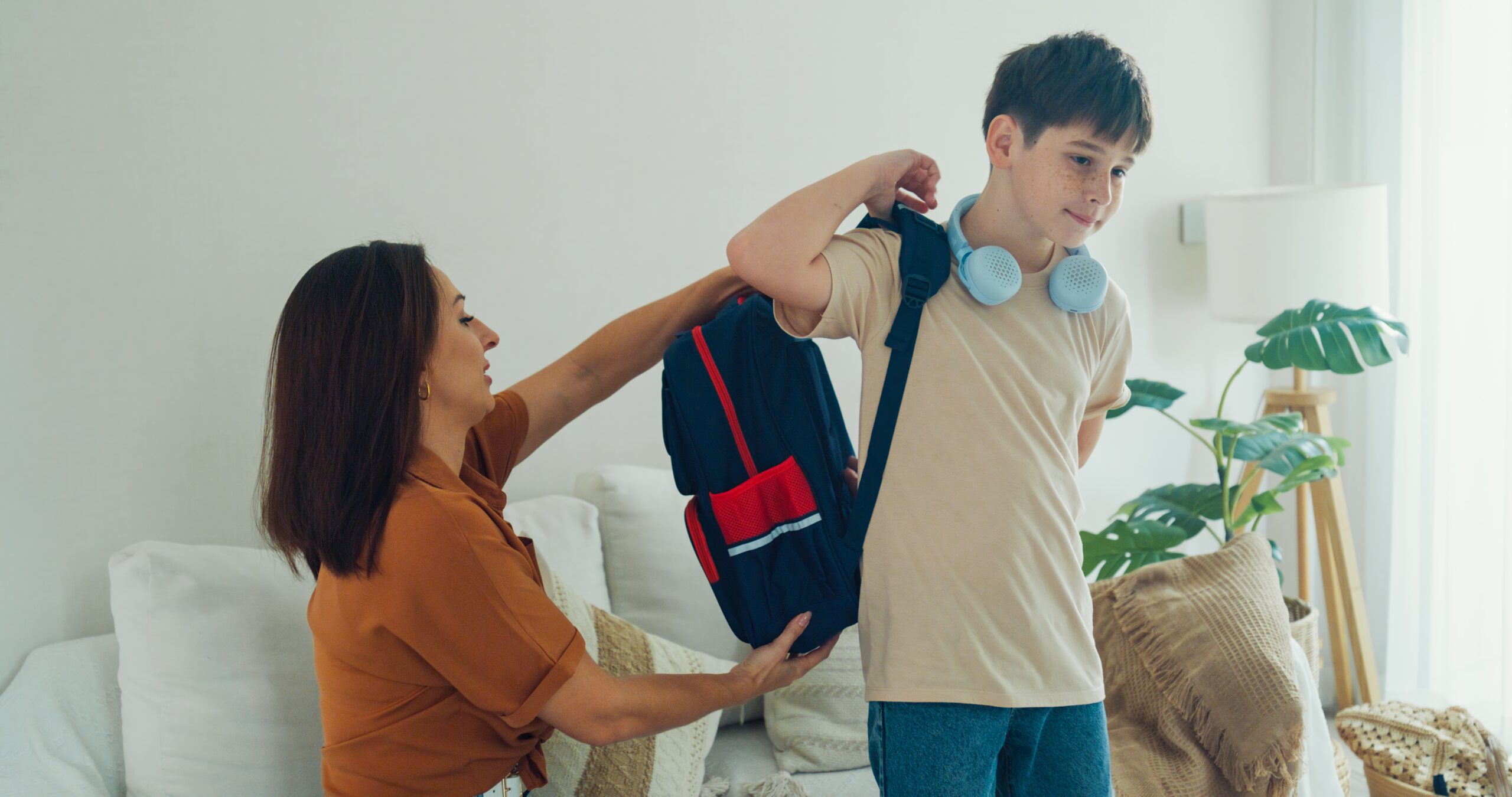 Young mother helps her son prepare his backpack in the living room for school