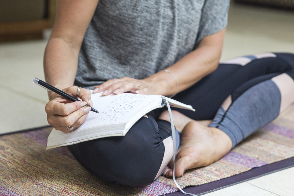 Woman writing in diary sitting cross-legged on exercise mat at home
