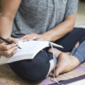 Woman writing in diary sitting cross-legged on exercise mat at home
