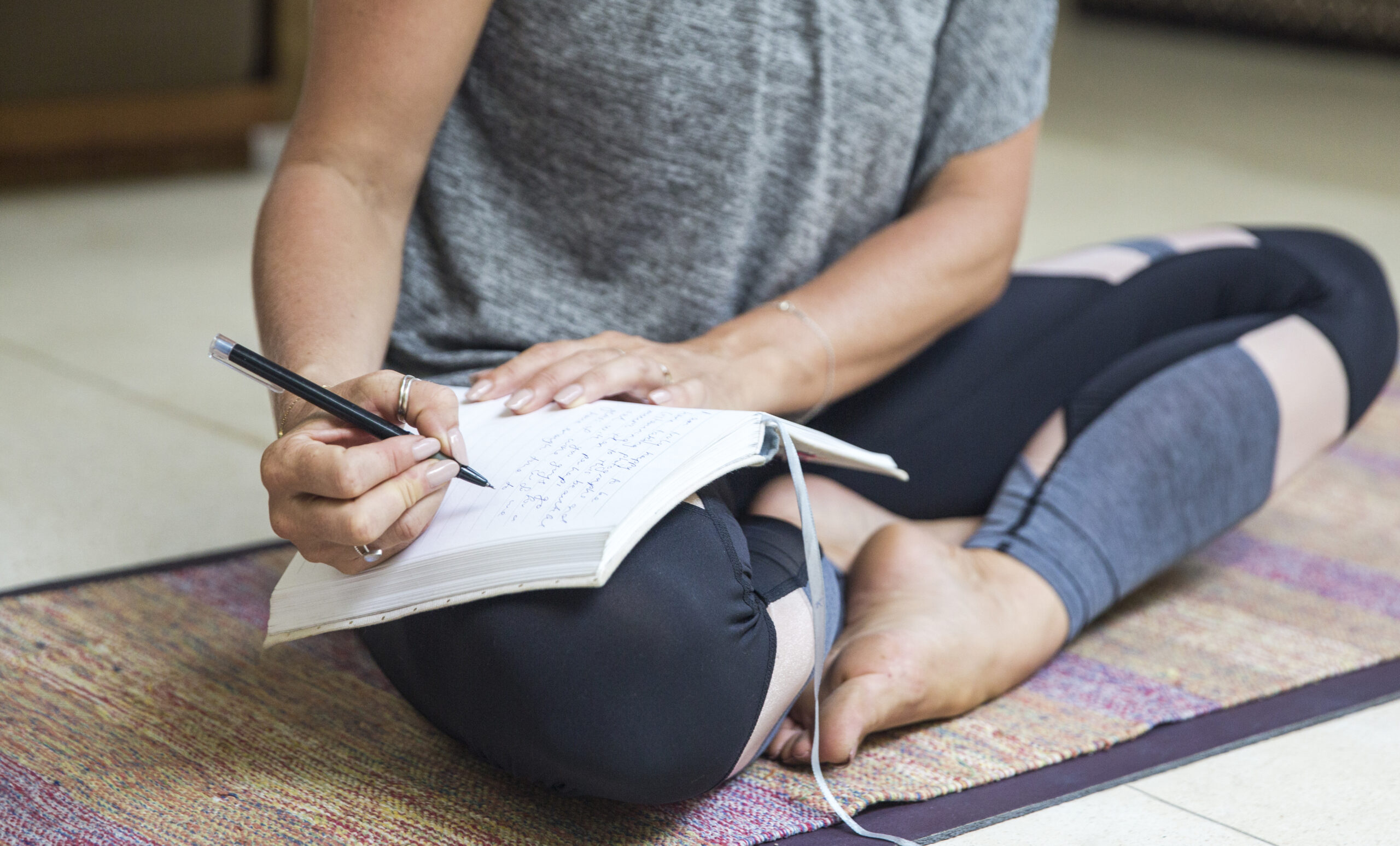 Woman writing in diary sitting cross-legged on exercise mat at home