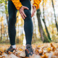 Close-up image of runner athlete dressed sporty on the running path standing and feeling acute knee pain while morning jogging in yellow autumn park